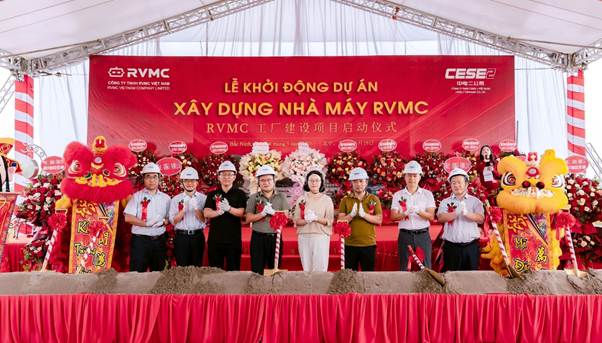 Officials in hard hats and formal dress perform a groundbreaking ceremony on a red stage backdrop for the RVMC project, flanked by lion dance figures.